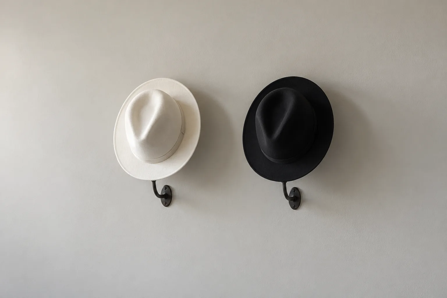 Due cappelli di feltro identici appesi a una parete grigia, uno bianco e uno nero