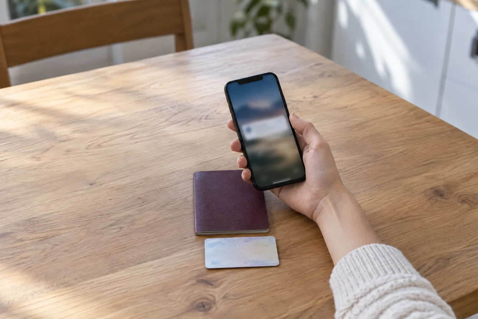 Una mano tiene uno smartphone con un messaggio in arrivo, sul tavolo un passaporto e una carta d'identità